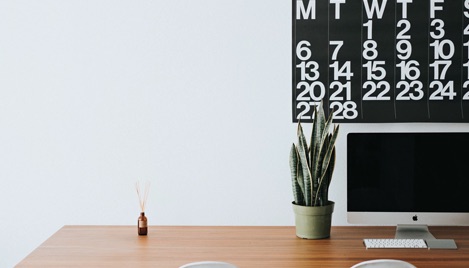 Minimalist desk scene with calendar, computer and plant.