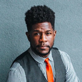 Professional headshot of a man in grey vest with orange tie.
