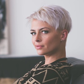 Professional headshot of a woman with a short blond pixie haircut.
