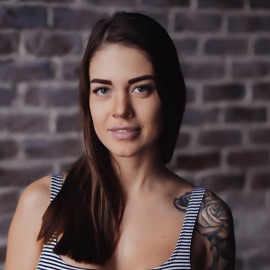Headshot of a woman with long brown hair and a tattoo on her shoulder.