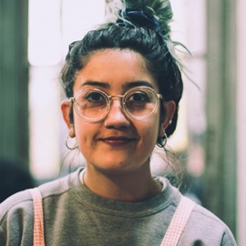 Casual headshot of a woman wearing a pink apron over her sweatshirt.